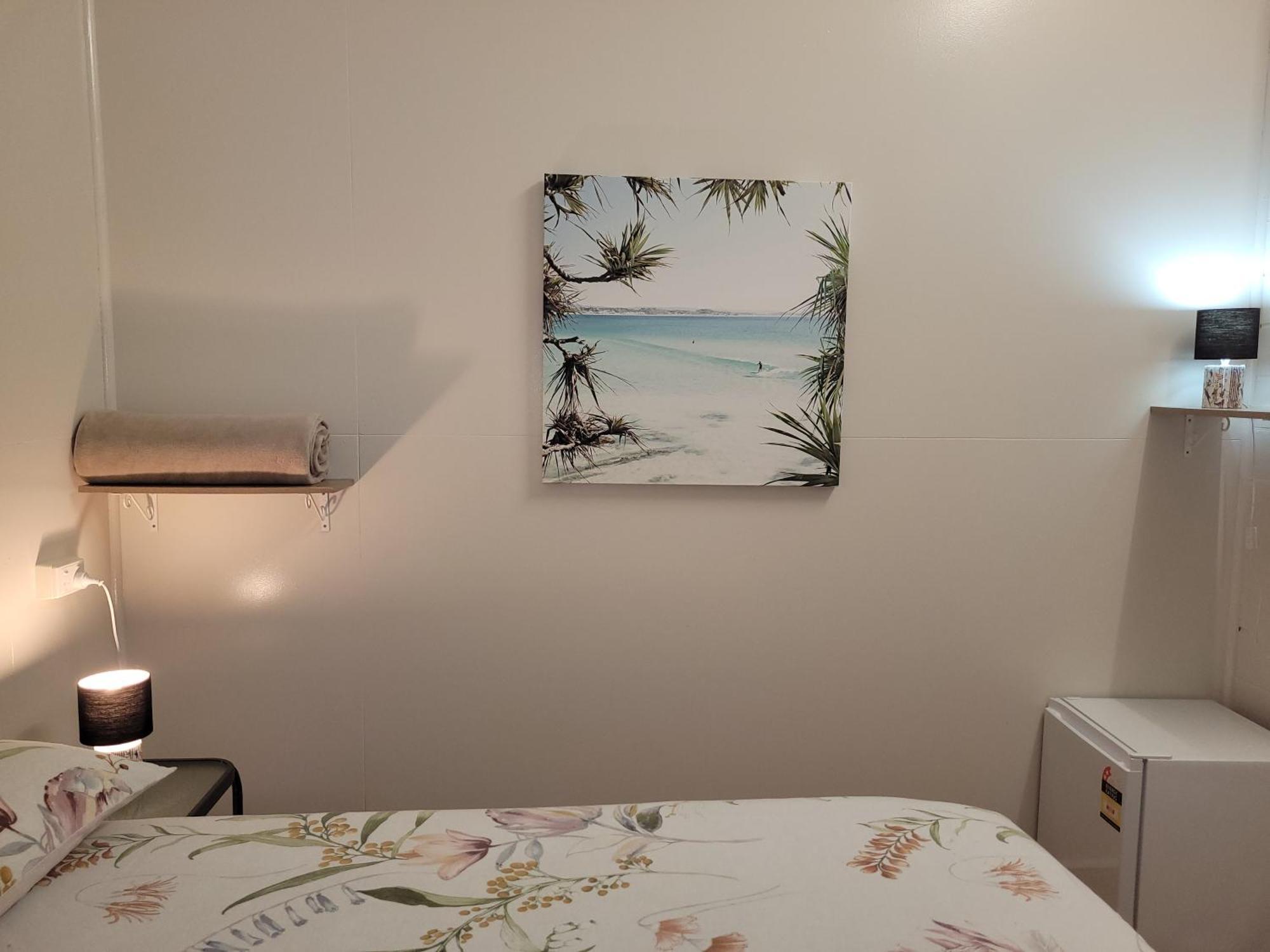 Travellers Paradise Κερνς Εξωτερικό φωτογραφία A photograph of a bedroom with a bed, a nightstand, a lamp, a painting, and a television